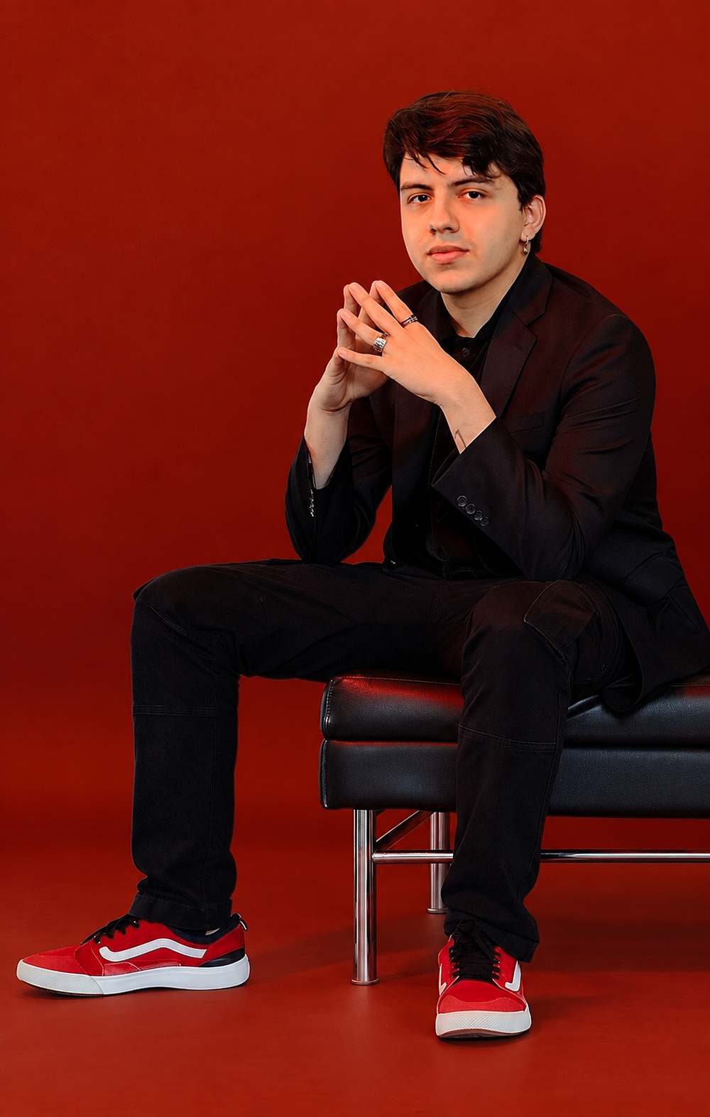 Jose Fonseca seated in a black suit and red sneakers against a red background